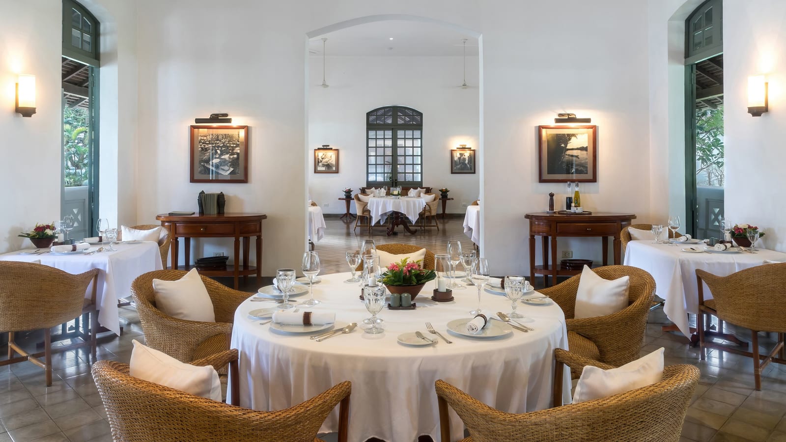 La sala di un ristorante apparecchiata prima del servizio, con i tavoli rotondi e le sedie in vimini